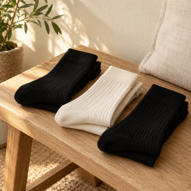 Gefaltete schwarze und weiße Socken auf einer Holzbank.